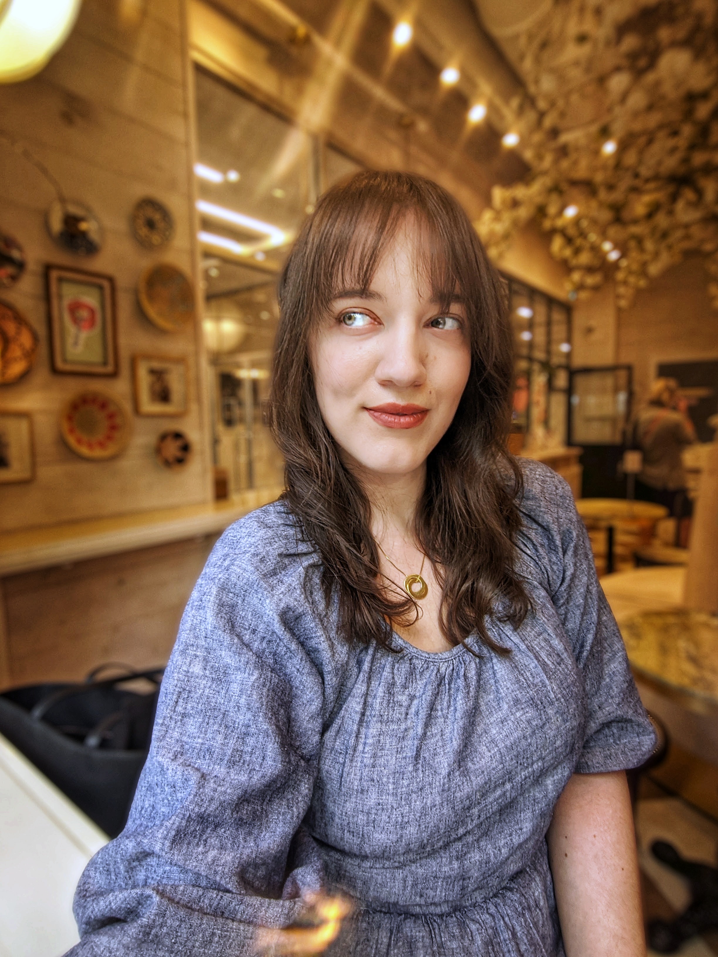 A headshot of Sage Franch, sitting in a public space and looking off to the side.